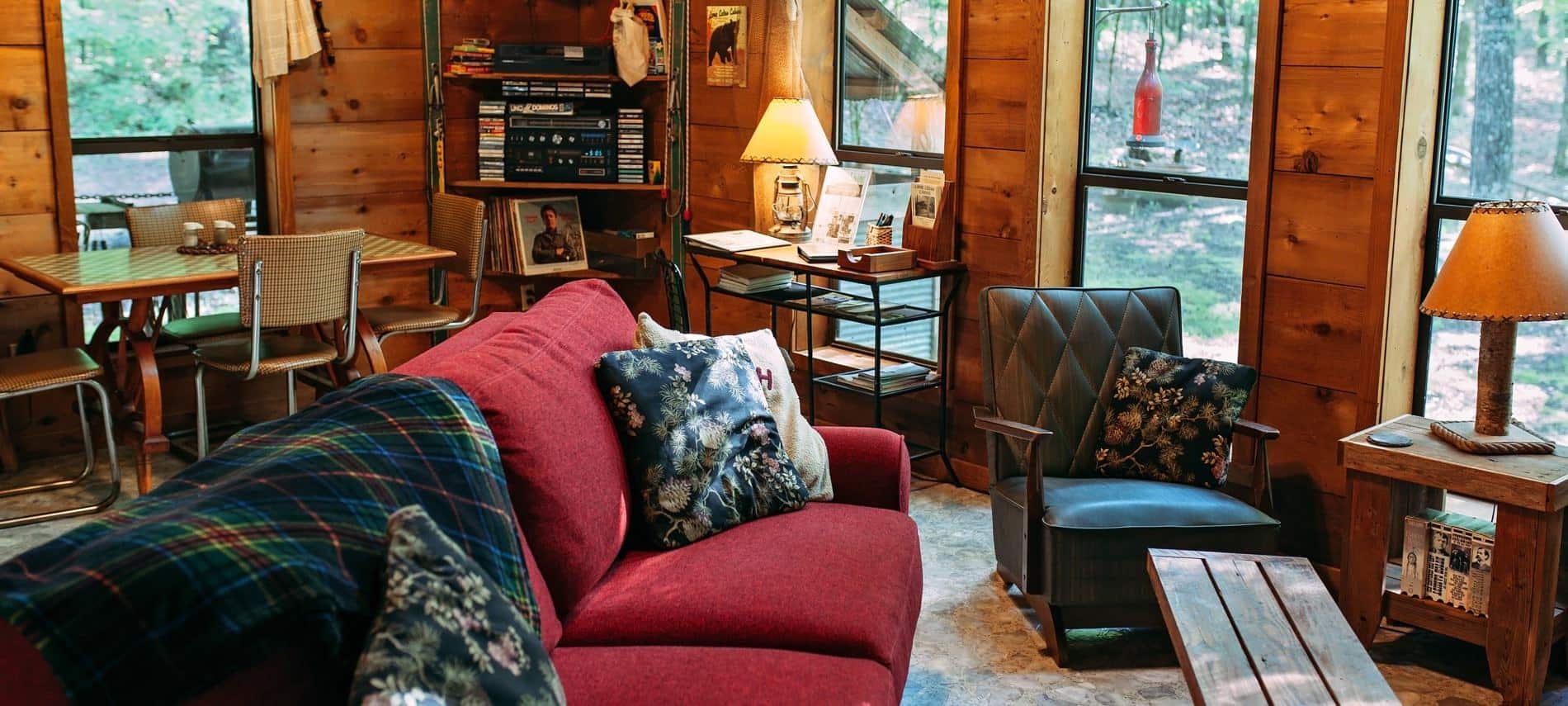 Inside of wood cabin with lots of windows, dining table, and cozy living area with sofa, chair and tables