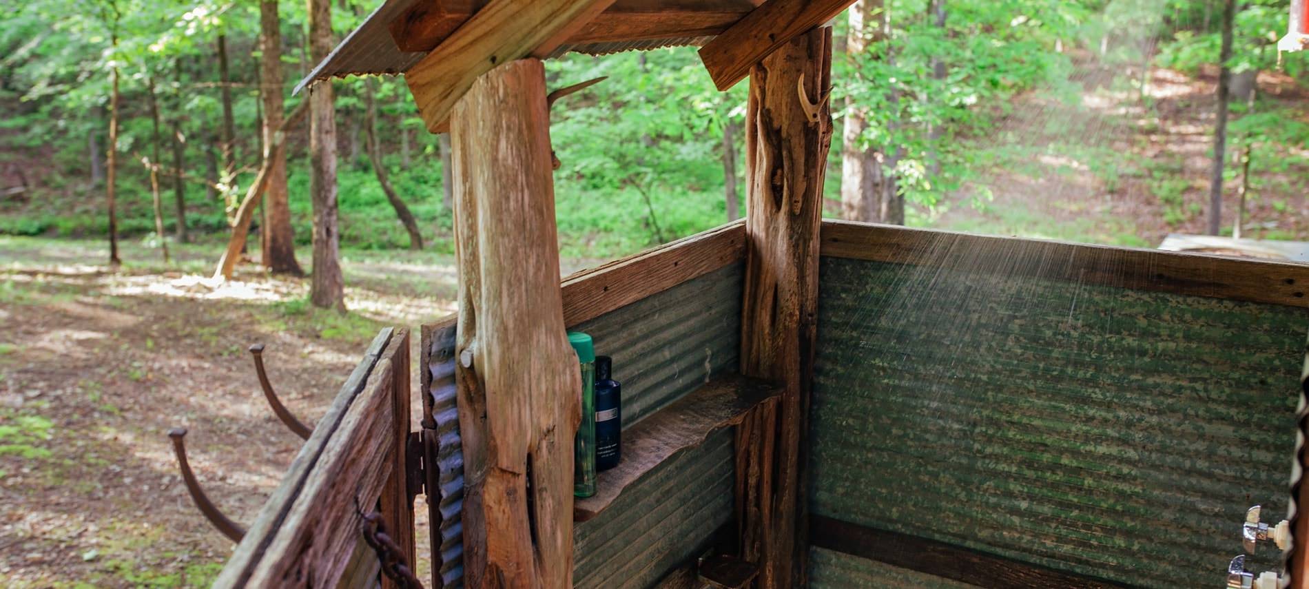 Outdoor shower with metal and wood walls amidst beautiful wooded views