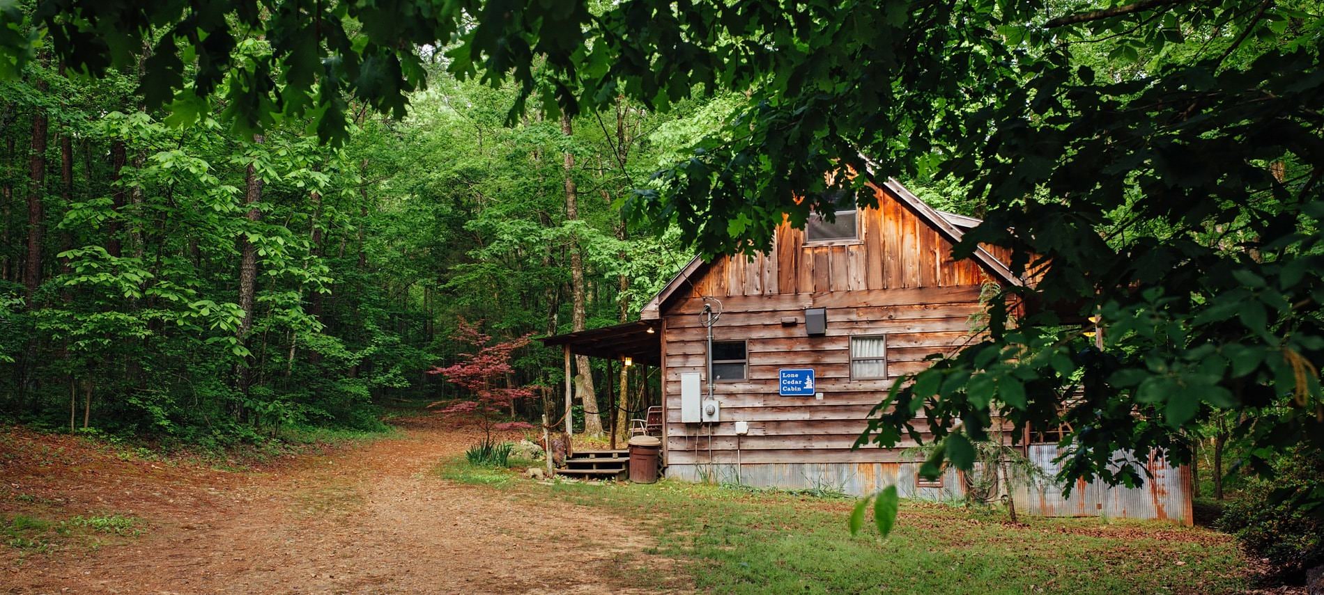 Exterior view of wooded cabin, side covered porch, surrounded by lush green trees