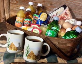 Brown basket filled with juice, tea, bacon, eggs, and more, with two cups of coffee set in front