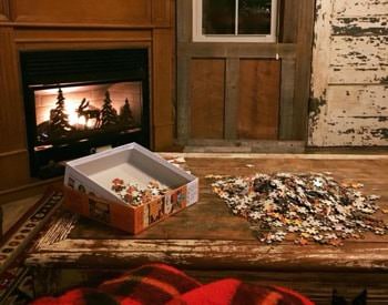 Interior of cabin with glowing corner fireplace and a puzzle on top of a rustic coffee table