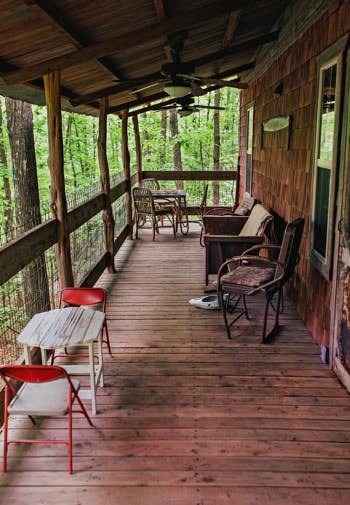 Covered side porch with various tables and chairs and a view of the woods