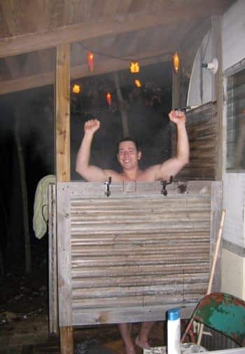 Smiling man standing inside an outdoor shower on the side of the cabin