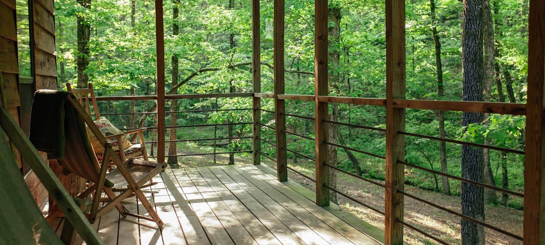 Exterior cabin view of side covered porch surrounded by green leafy trees